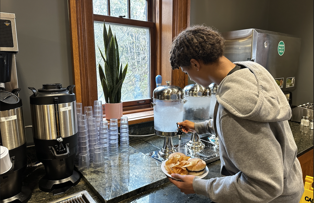A student pours himself a glass of water. On his plate are potato chips and a hamburger.